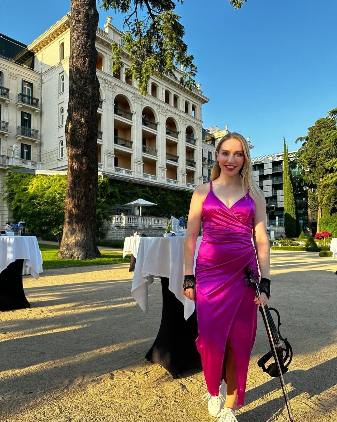 Violinski nastop iz repertoarja — violinistka v rožnati obleki z električno violino pred zgodovinsko graščino; glasba za poroko